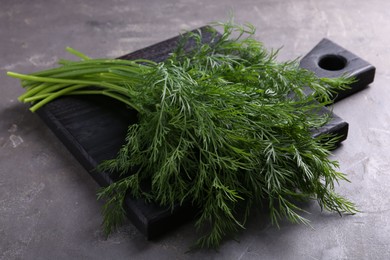 Photo of Board with sprigs of fresh dill on grey textured table, closeup