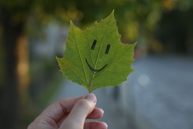 Woman holding green leaf with smiley face outdoors, closeup