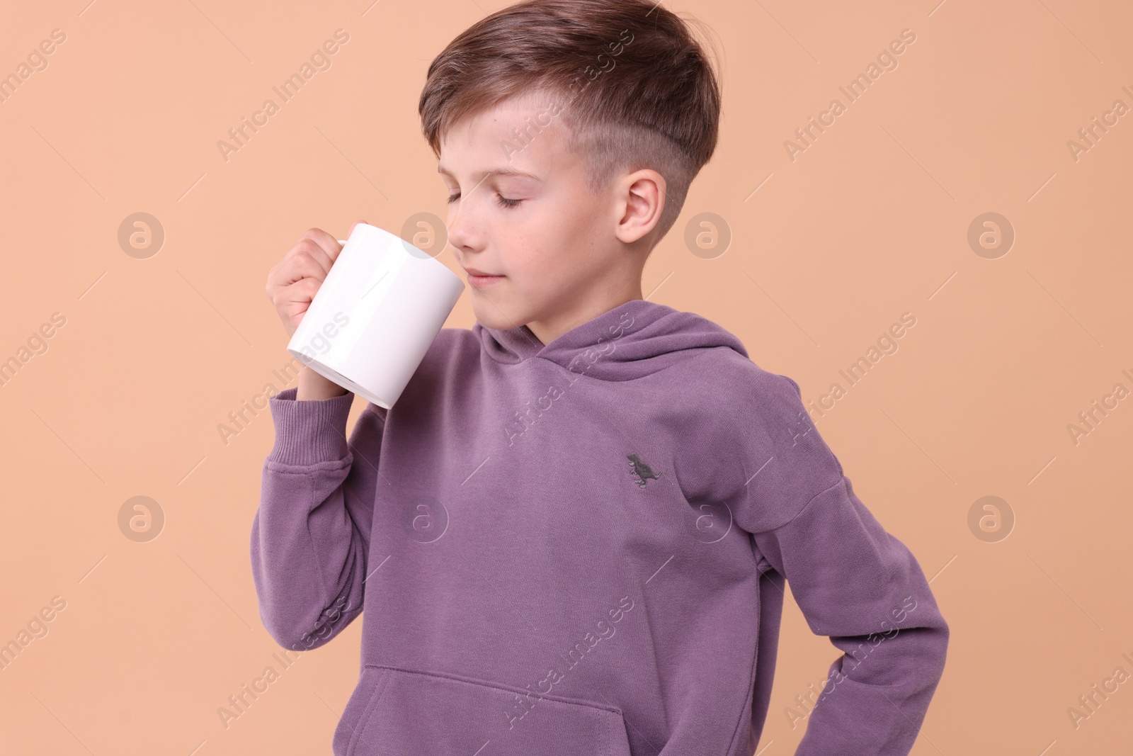 Photo of Cute boy drinking beverage from white ceramic mug on beige background