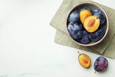 Photo of Tasty ripe plums on white marble table, flat lay. Space for text