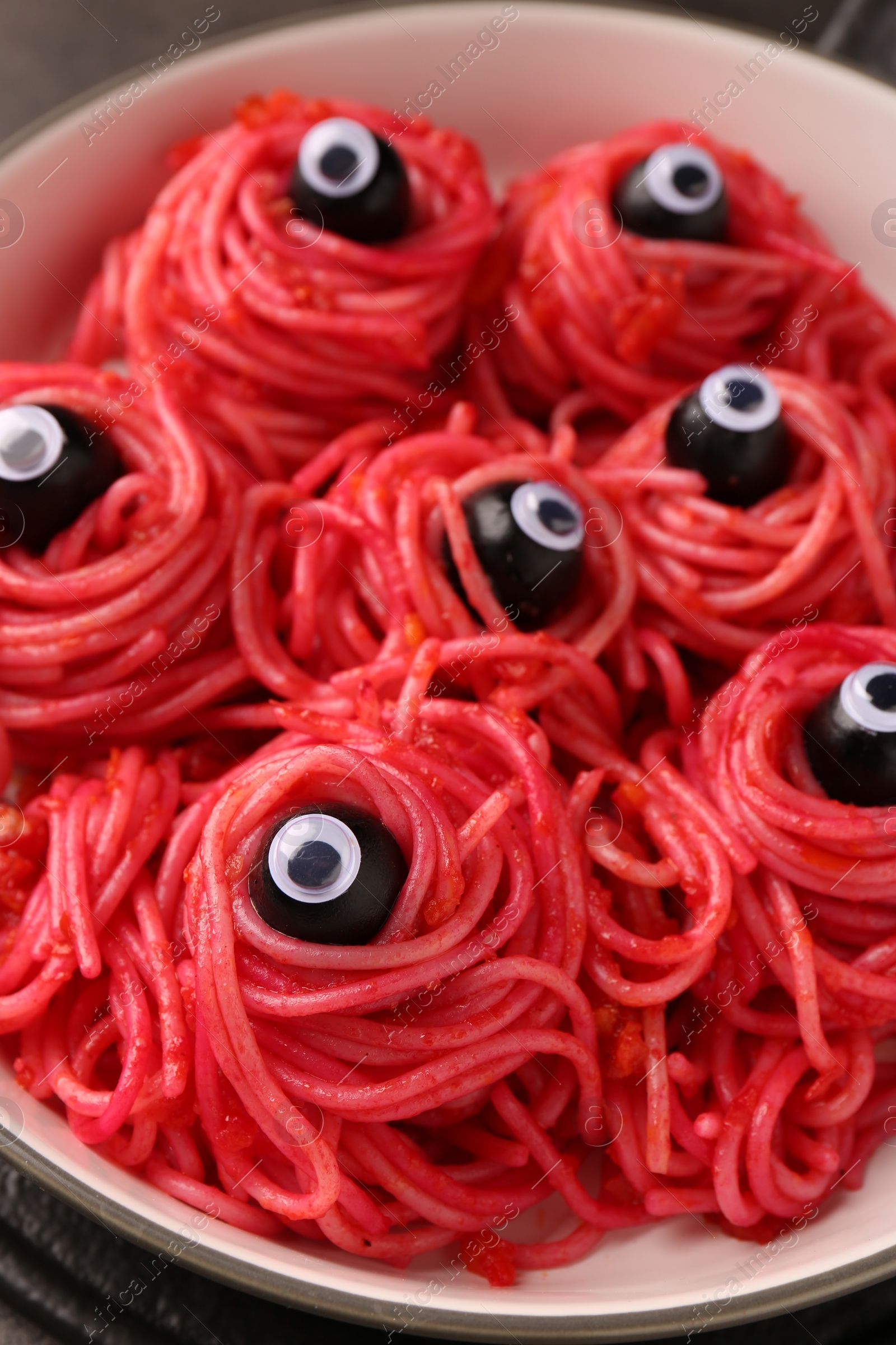 Photo of Red pasta with decorative eyes and olives in bowl on table, closeup. Halloween food