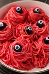 Red pasta with decorative eyes and olives in bowl on table, closeup. Halloween food