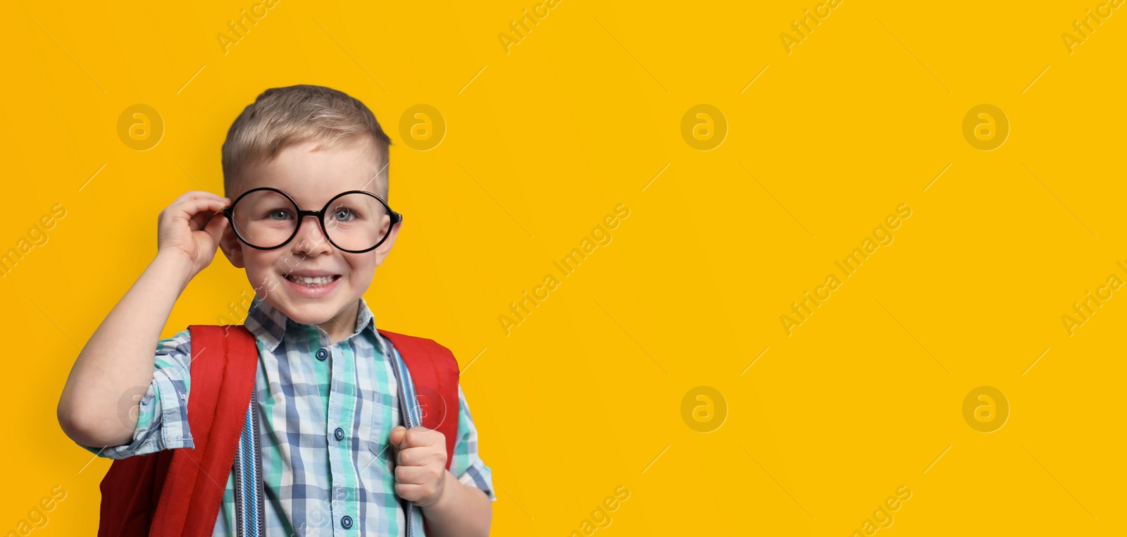 Image of First time at school. Cute little child wearing glasses on yellow background, space for text. Banner design