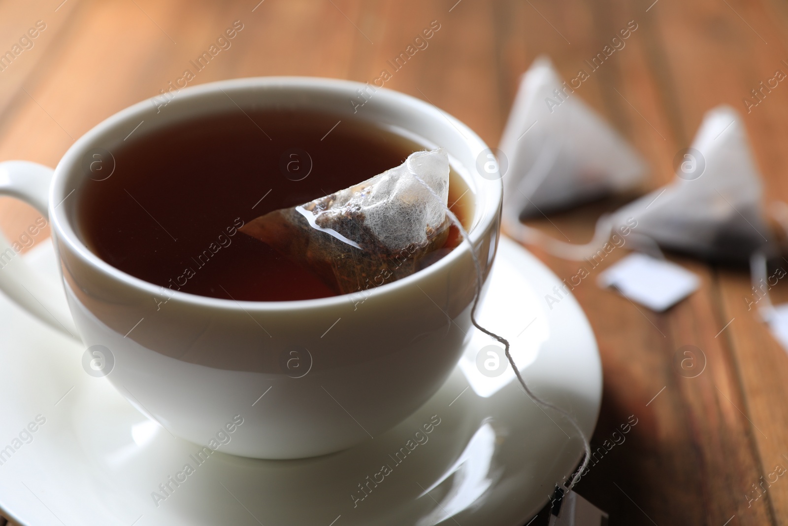 Photo of Tea bag in cup on wooden table, closeup