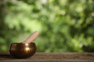 Photo of Golden singing bowl with mallet on wooden table outdoors, space for text