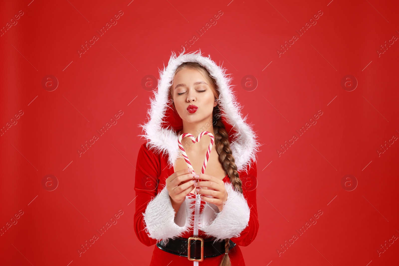 Photo of Beautiful Santa girl with candy canes on red background. Christmas eve