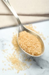 Photo of Spoon with brown sugar on white marble table, closeup