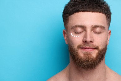 Photo of Handsome man with moisturizing cream on his face against light blue background, space for text