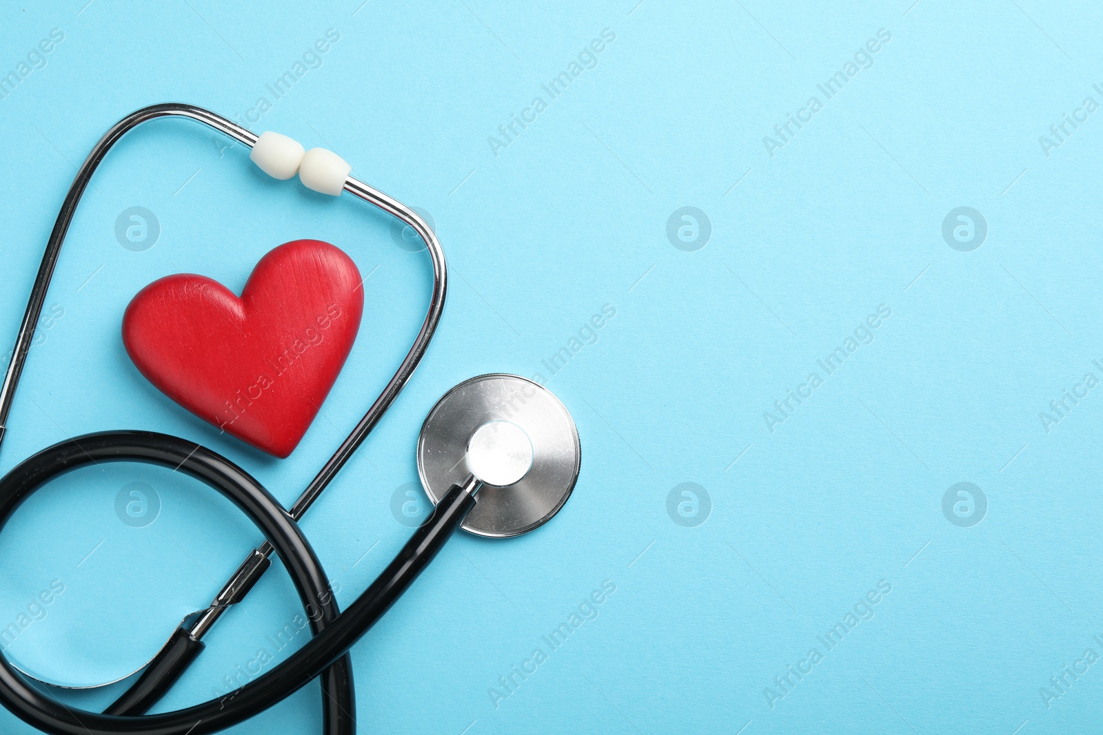 Photo of Stethoscope and red heart on light blue background, top view. Space for text