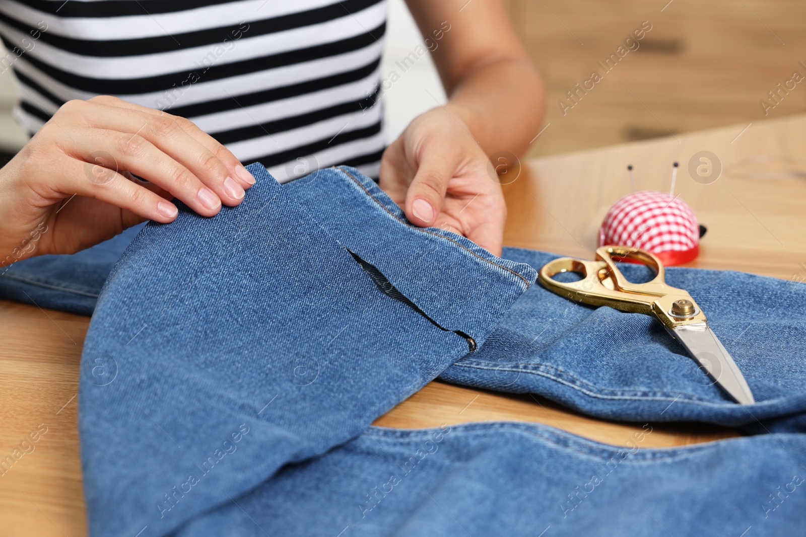 Photo of Young woman shortening jeans at wooden table, closeup