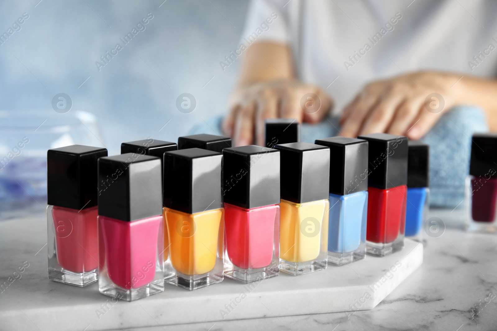 Photo of Bottles of bright nail polish and blurred woman on background