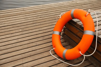 Photo of Orange lifebuoy on wooden pier, space for text. Rescue equipment