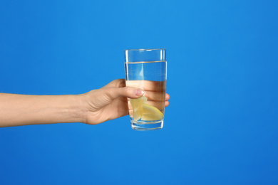 Young woman with glass of lemon water on light blue background, closeup