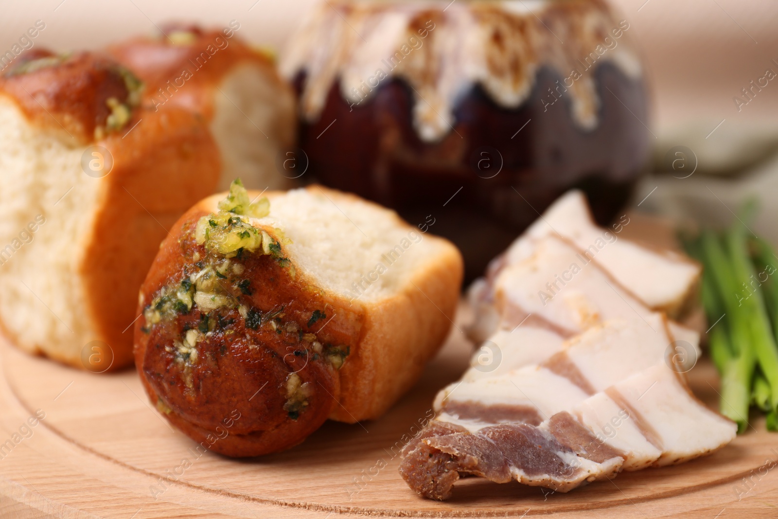 Photo of Delicious pampushky (buns with garlic), salo and green onions on wooden board, closeup