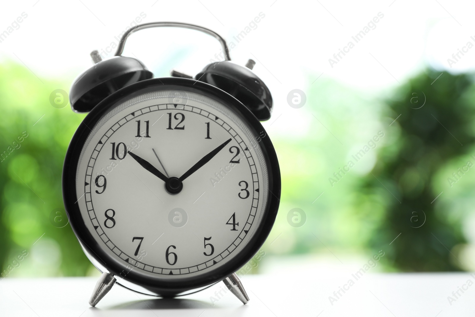 Photo of Modern black alarm clock on white table against blurred background. Space for text