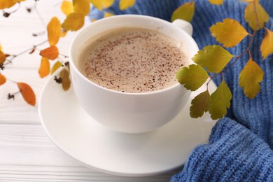 Cup of hot drink, leaves and knitted sweater on white wooden table, closeup. Cozy autumn atmosphere