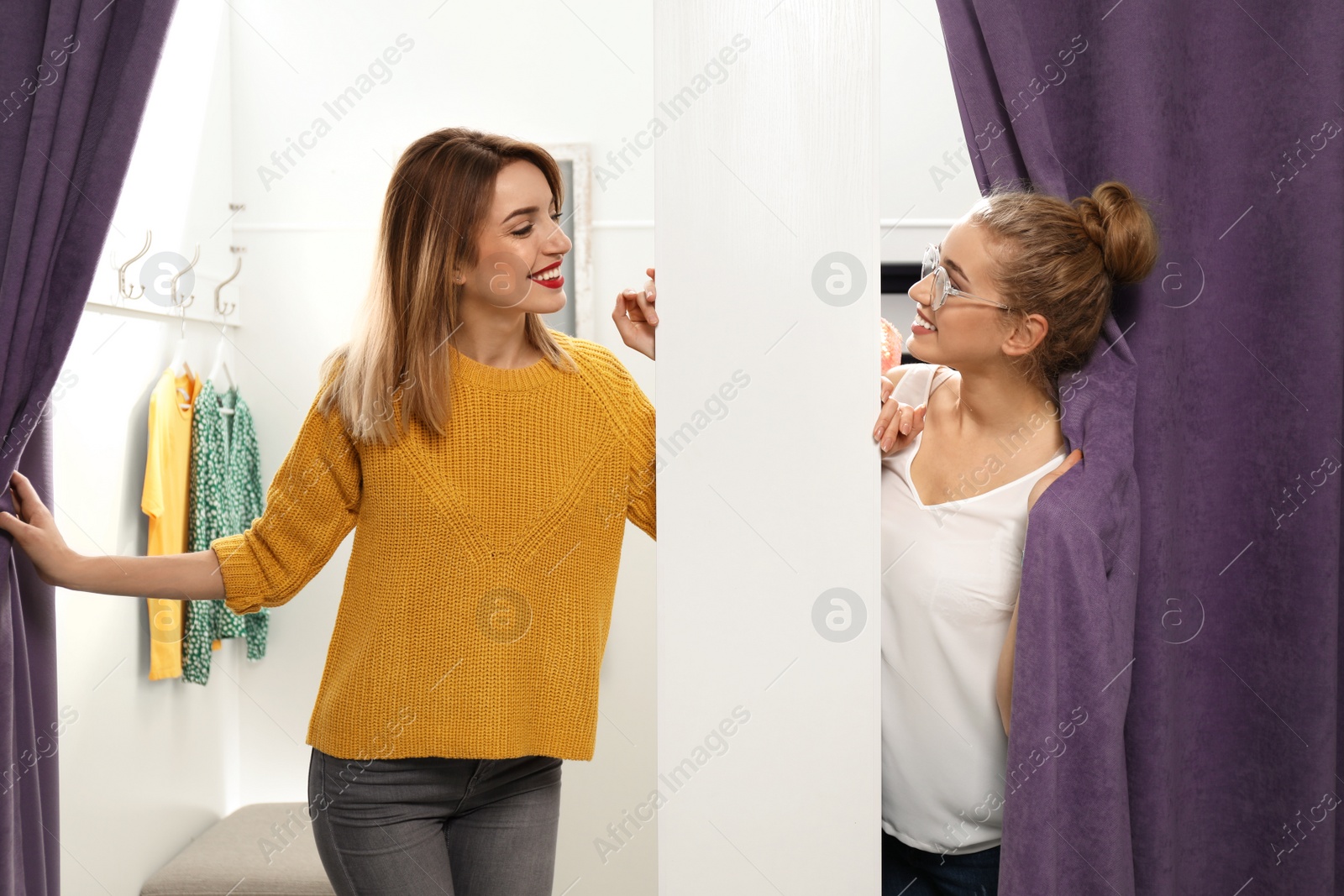 Photo of Young woman with her friend in dressing rooms. Fashion store