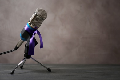 Photo of Microphone with purple awareness ribbon on table against brown background, space for text