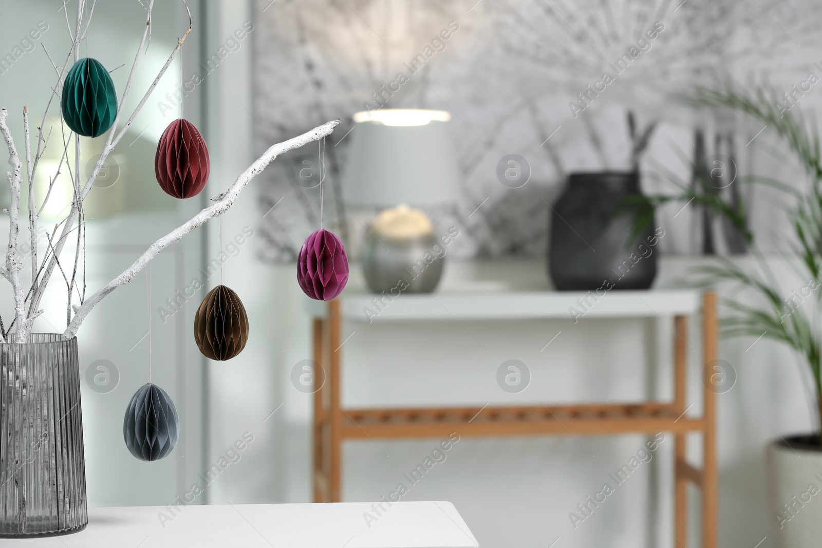 Photo of Branches with paper eggs in vase on white table at home, space for text. Beautiful Easter decor