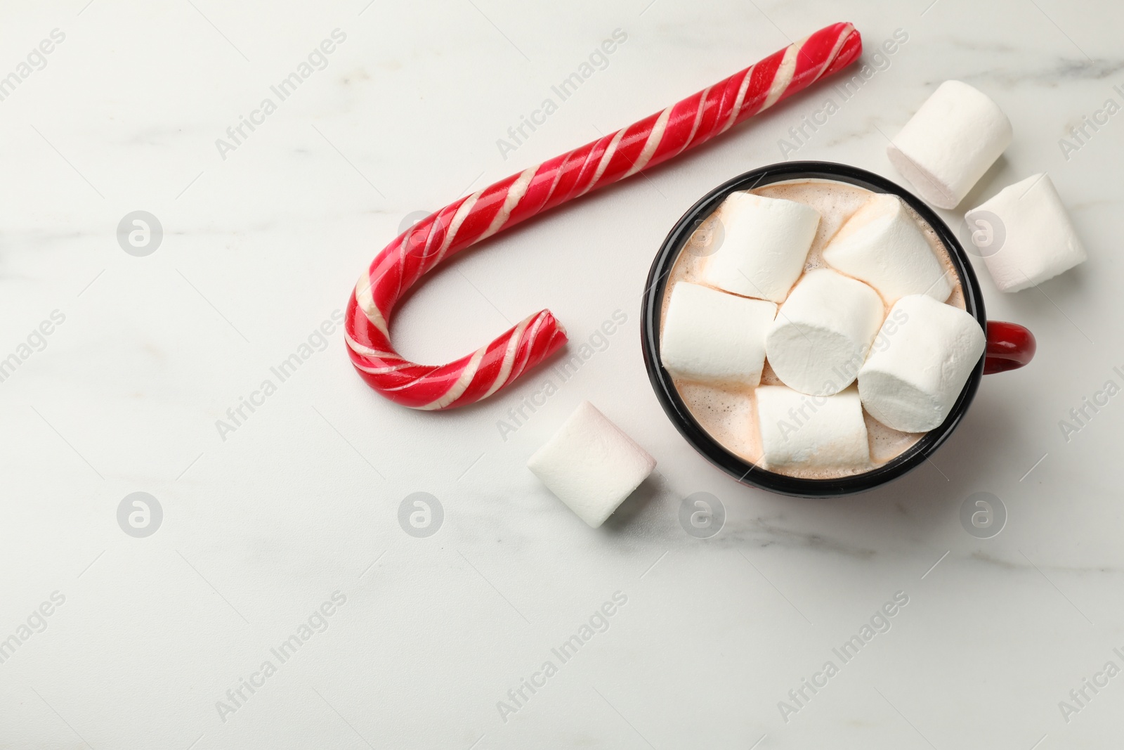 Photo of Tasty hot chocolate with marshmallows and candy cane on white marble table, top view. Space for text