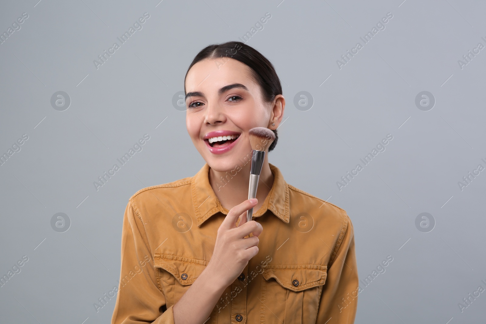 Photo of Happy woman with makeup brush on light grey background