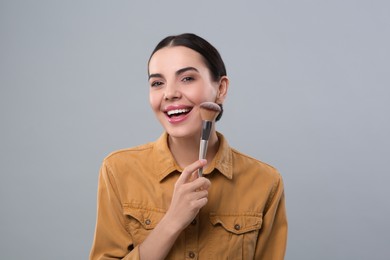 Photo of Happy woman with makeup brush on light grey background