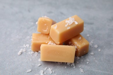 Yummy caramel candies and sea salt on grey table, closeup