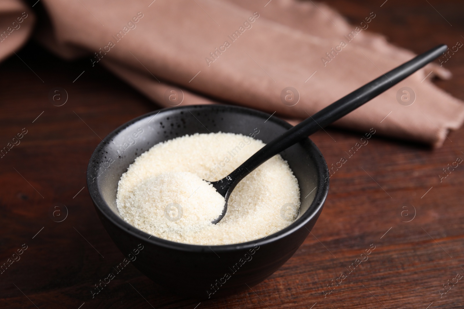 Photo of Black bowl with gelatin powder and spoon on wooden table, closeup