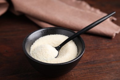 Black bowl with gelatin powder and spoon on wooden table, closeup