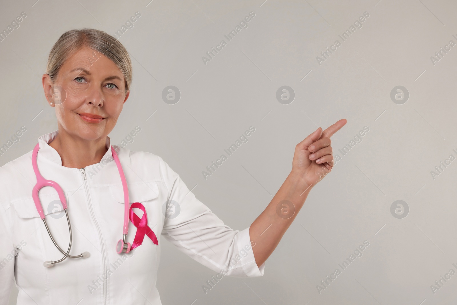 Photo of Doctor with pink ribbon and stethoscope on light grey background, space for text. Breast cancer awareness