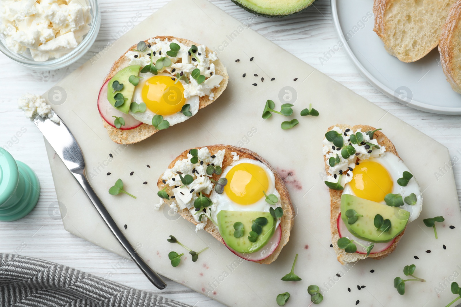 Photo of Delicious sandwiches with egg, cheese, avocado and microgreens on white wooden table, flat lay