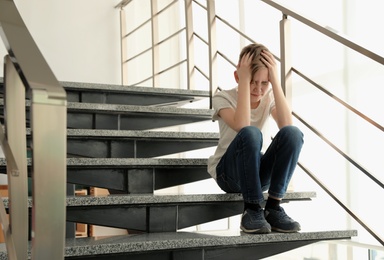 Photo of Sad little boy sitting on stairs indoors