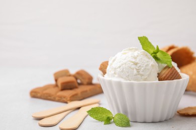 Scoops of tasty ice cream with mint leaves and caramel candies on white table, closeup. Space for text