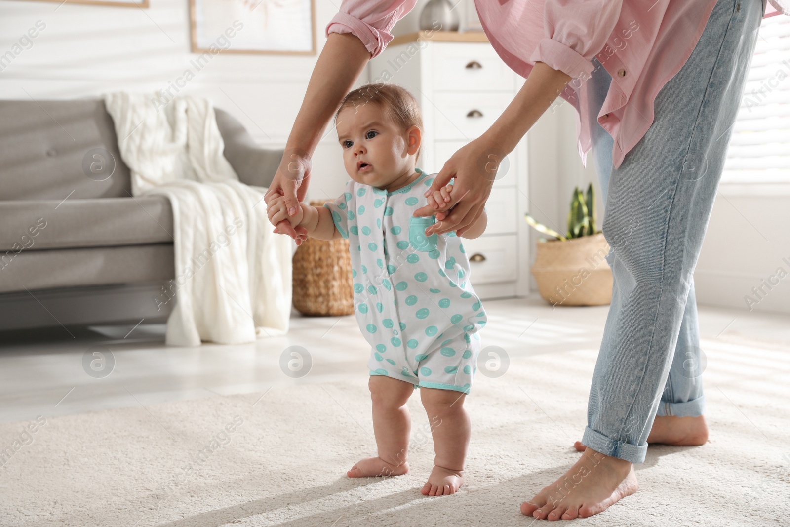 Photo of Mother supporting her baby daughter while she learning to walk at home