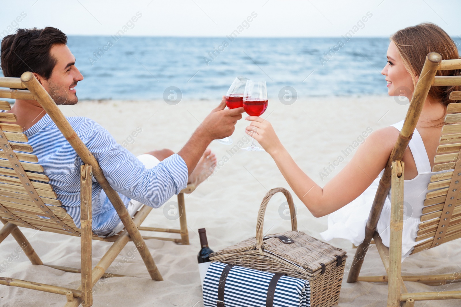 Photo of Happy young couple with glasses of wine sitting on deck chairs at sea beach