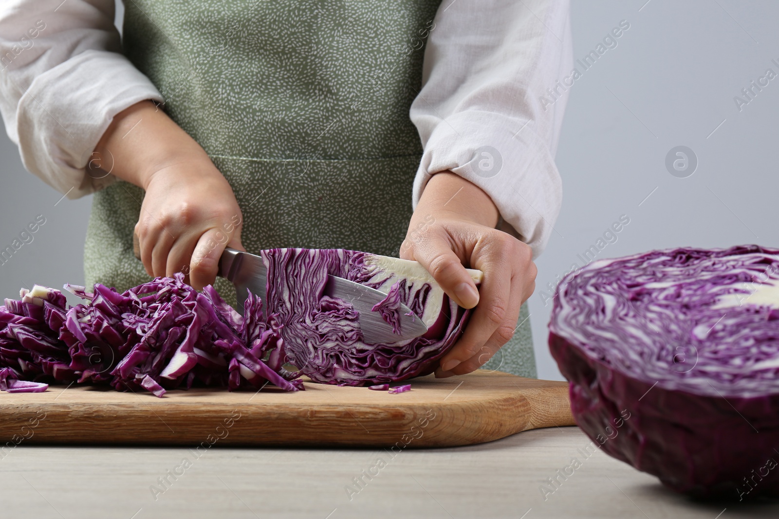 Photo of Woman cutting fresh radicchio cabbage on board at wooden table, closeup