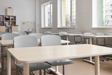 Photo of Empty school classroom with contemporary furniture and windows