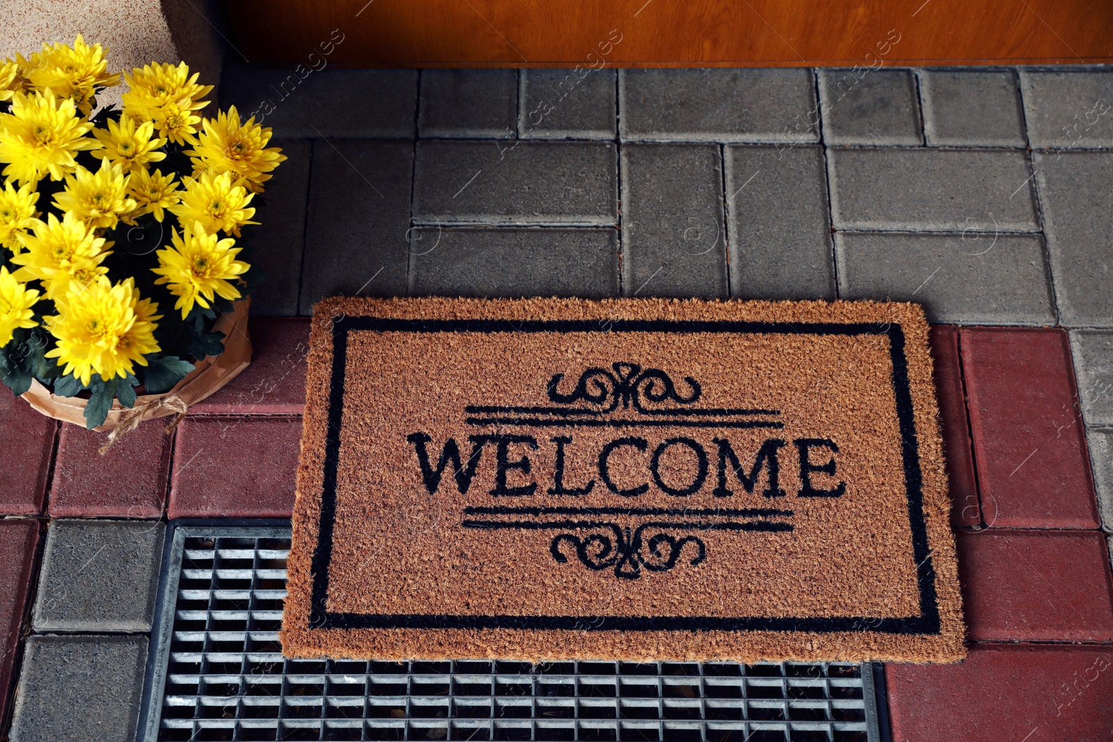 Photo of Door mat with word Welcome and beautiful flowers near entrance