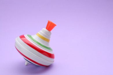 Photo of One bright spinning top on violet background, space for text. Toy whirligig
