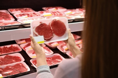 Photo of Woman taking packed pork meat from shelf in supermarket