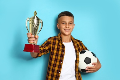 Photo of Happy boy with golden winning cup and soccer ball on blue background
