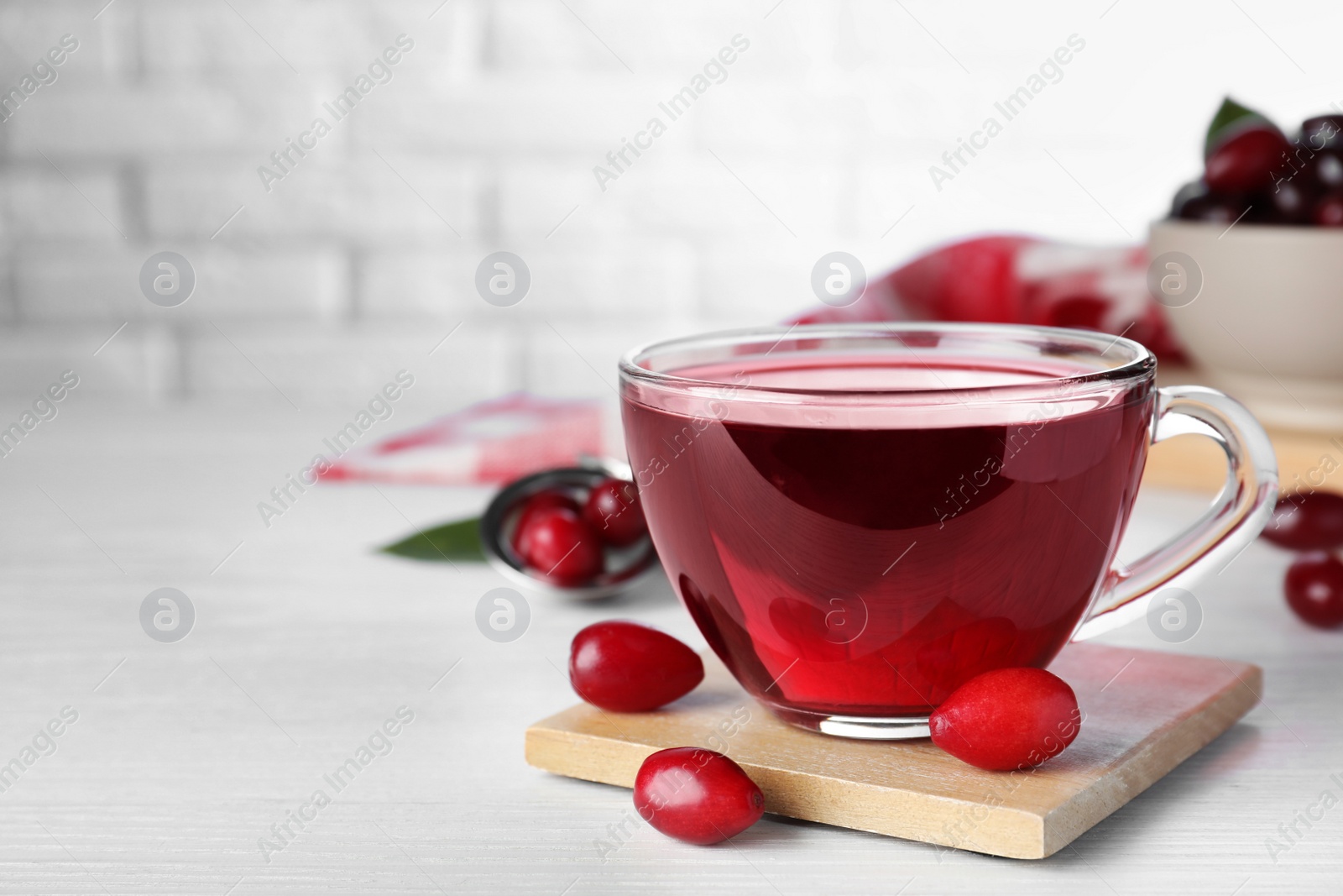 Photo of Glass cup of fresh dogwood tea and berries on white wooden table. Space for text