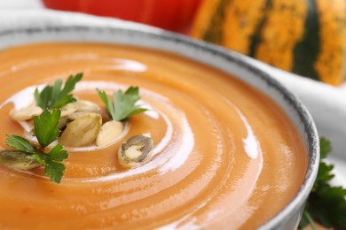 Delicious pumpkin soup with parsley and seeds in bowl, closeup