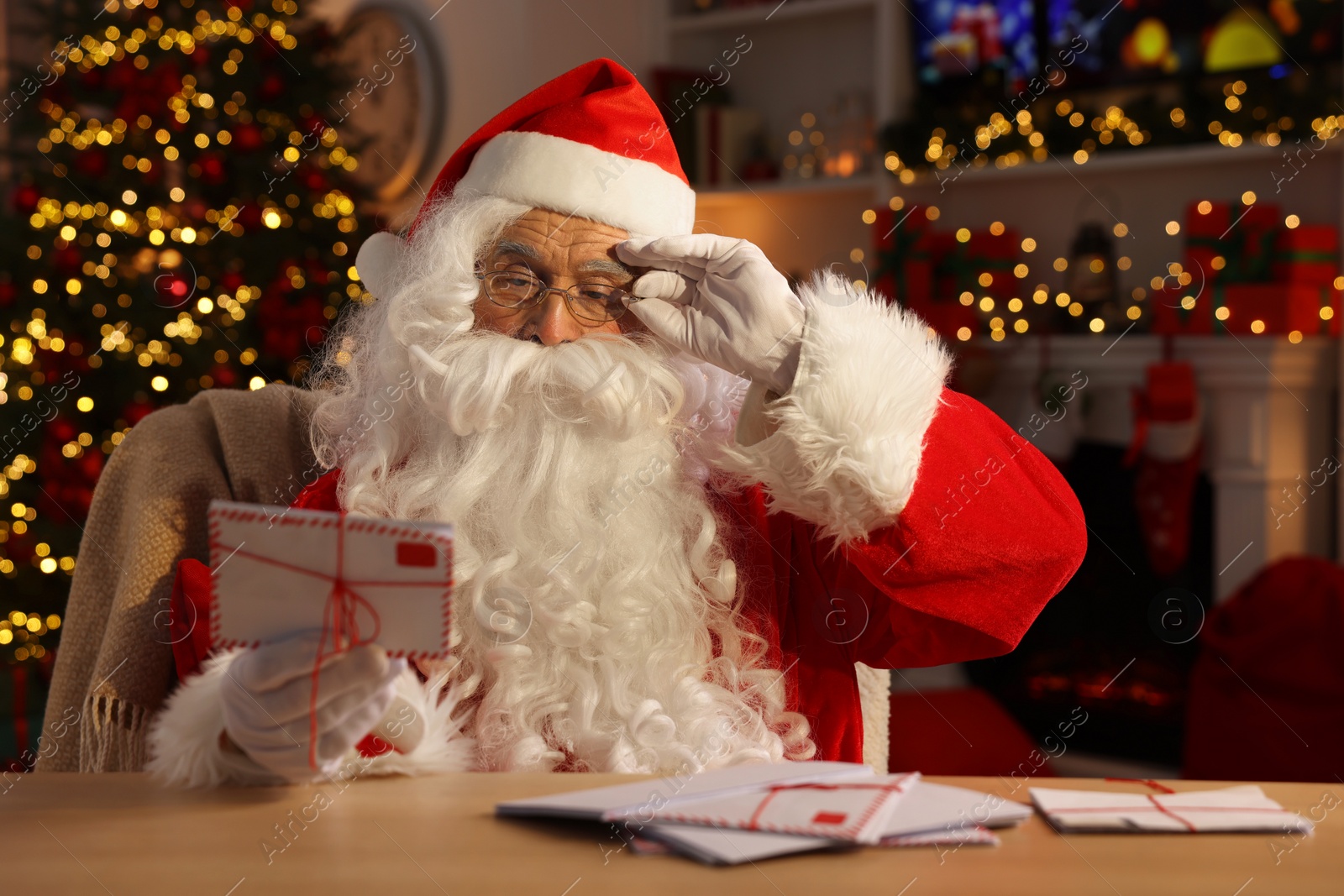 Photo of Santa Claus holding letter at table in room decorated for Christmas