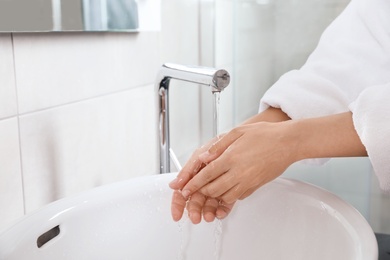 Photo of Woman washing hands over sink in bathroom, closeup. Using soap