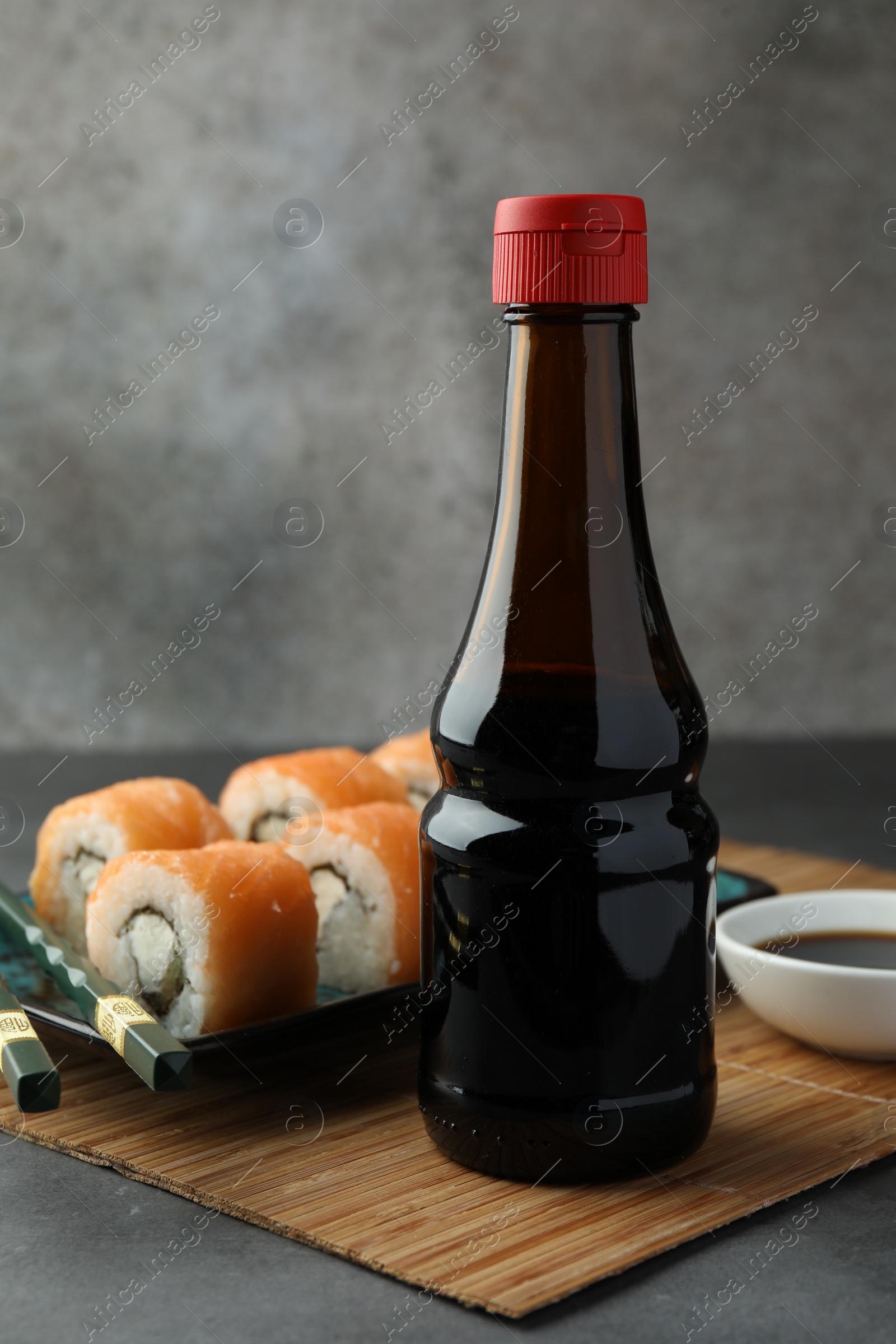 Photo of Tasty soy sauce and sushi rolls with salmon on grey table