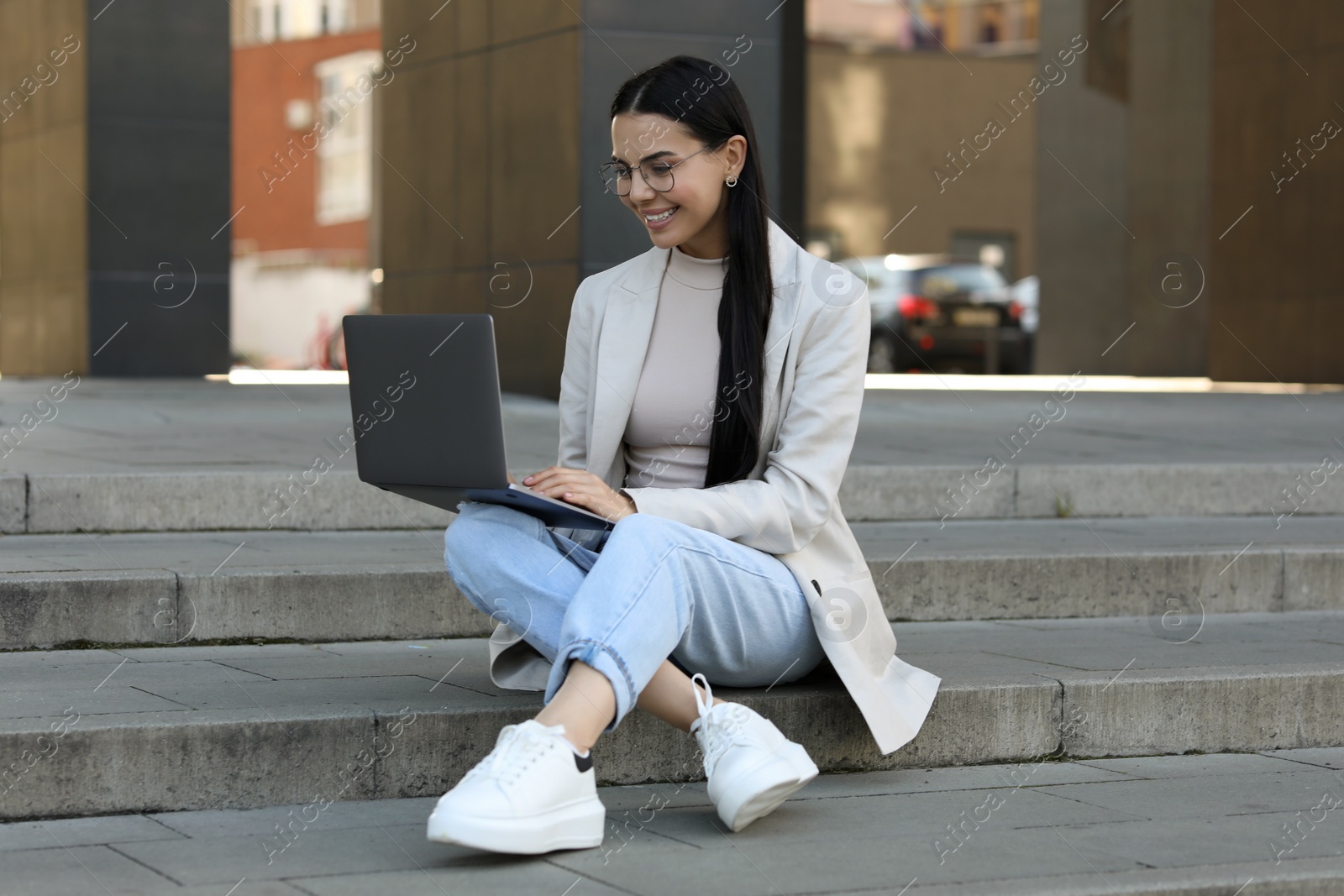 Photo of Happy young woman using modern laptop on stairs outdoors