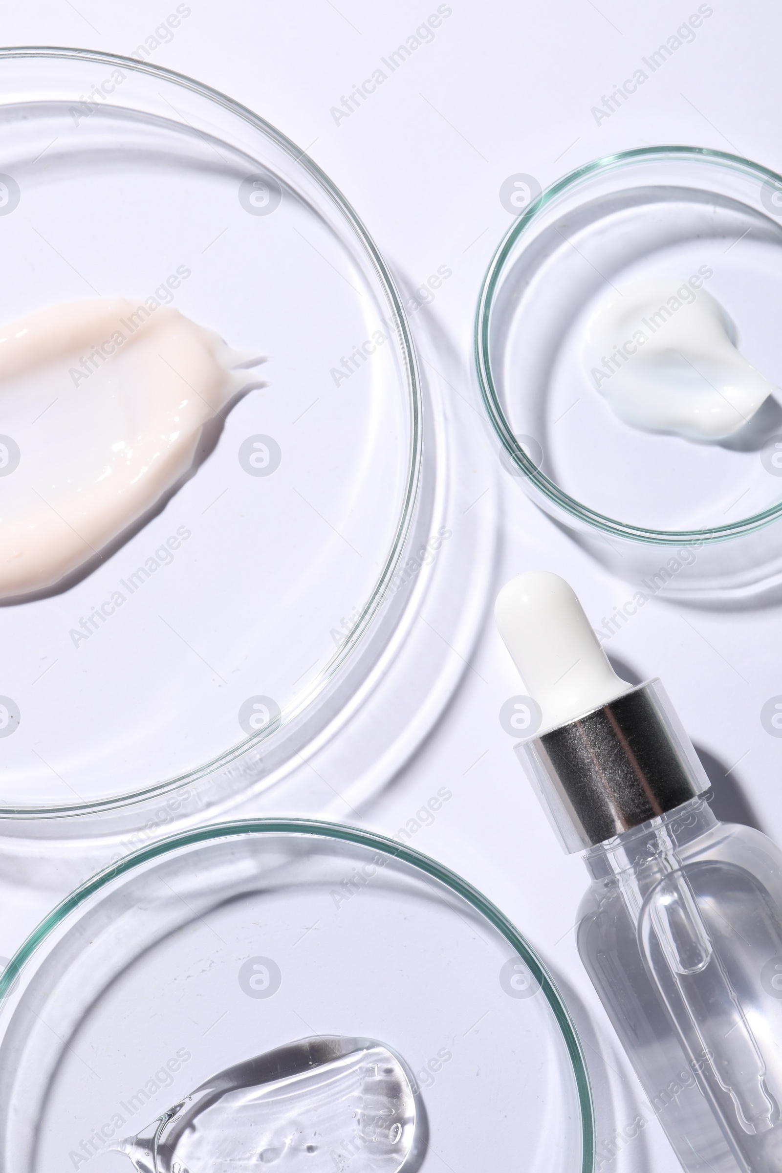 Photo of Petri dishes with samples of cosmetic serums and bottle on white background, flat lay