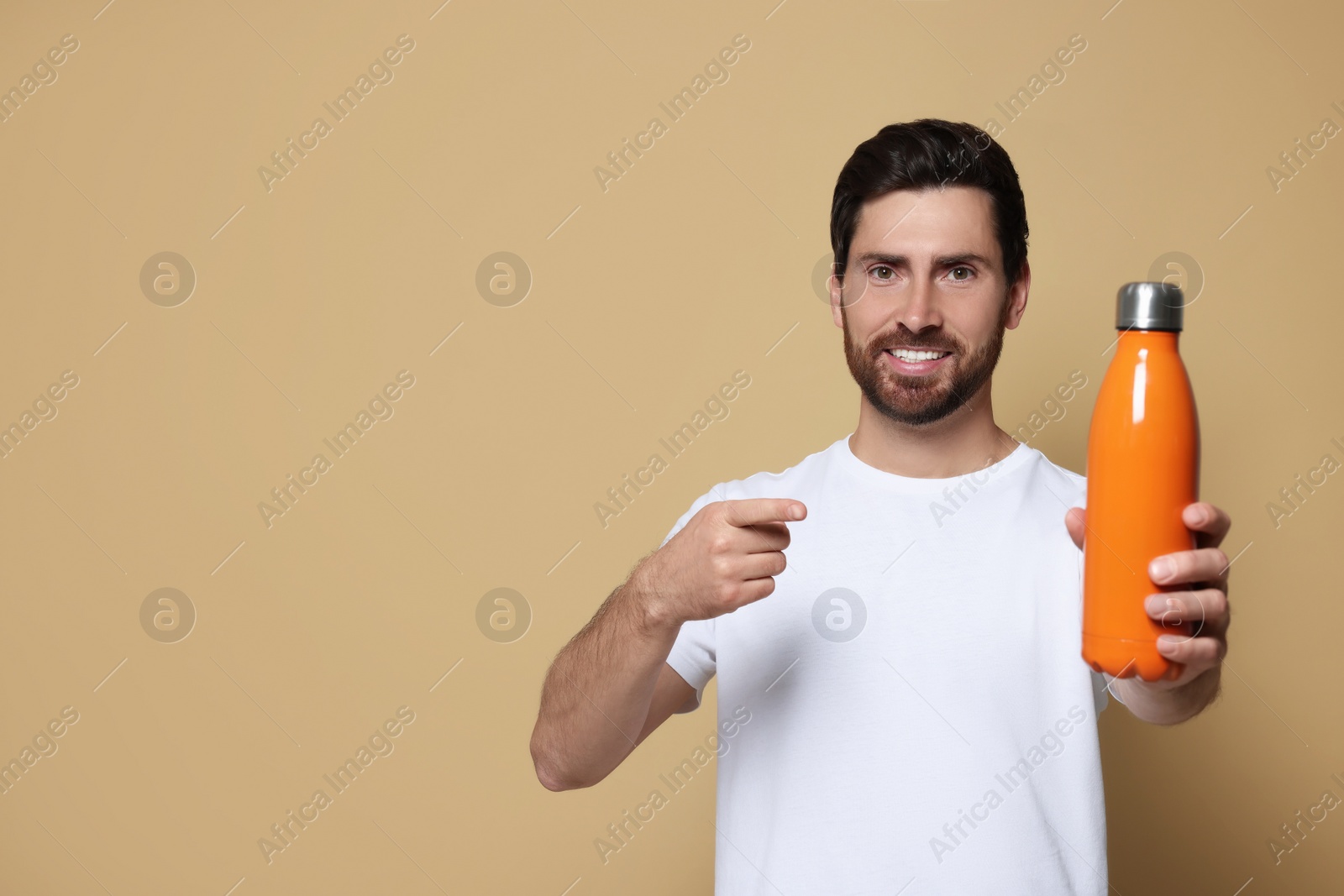 Photo of Man pointing at orange thermo bottle on beige background. Space for text