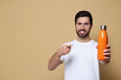 Man pointing at orange thermo bottle on beige background. Space for text